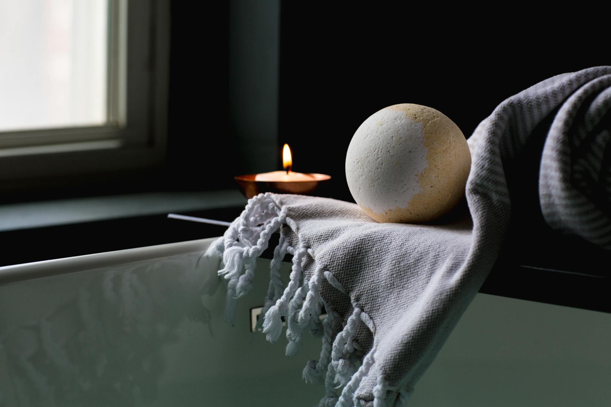 A serene spa setting with a bath bomb, candle, and towel on a dark elegant backdrop.